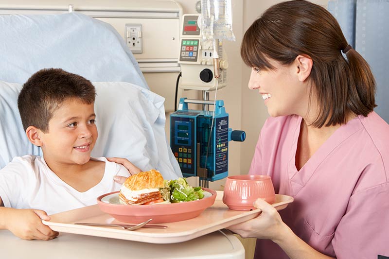 Krankenschwester serviert einem Jungen sein Mittagessen am Bett